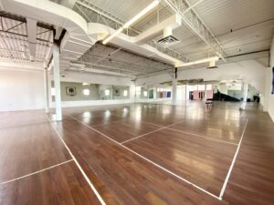 Open industrial flex space at 100 Symes Road Toronto with high ceilings, hardwood floors, exposed ductwork, and large mirrored walls