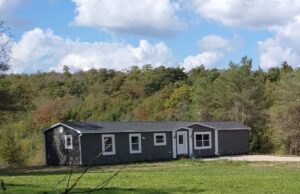 Single-storey rural home set on open land with forested hills and blue sky in the background