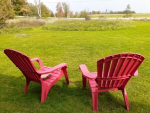 Two red Adirondack chairs on a grassy lawn overlooking open countryside and farmland