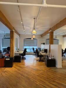 Open workspace in Unit 100 at 20 Maud Street Toronto featuring exposed brick, timber beams, hardwood floors, and flexible office layout
