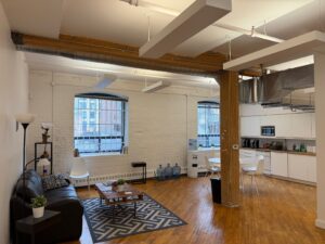 Kitchen and lounge area in Unit 100 at 20 Maud Street Toronto featuring exposed brick, timber beams, hardwood floors, and open-concept office space